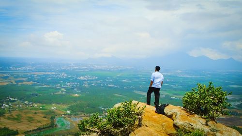 Rear view of man standing on mountain by sea against sky