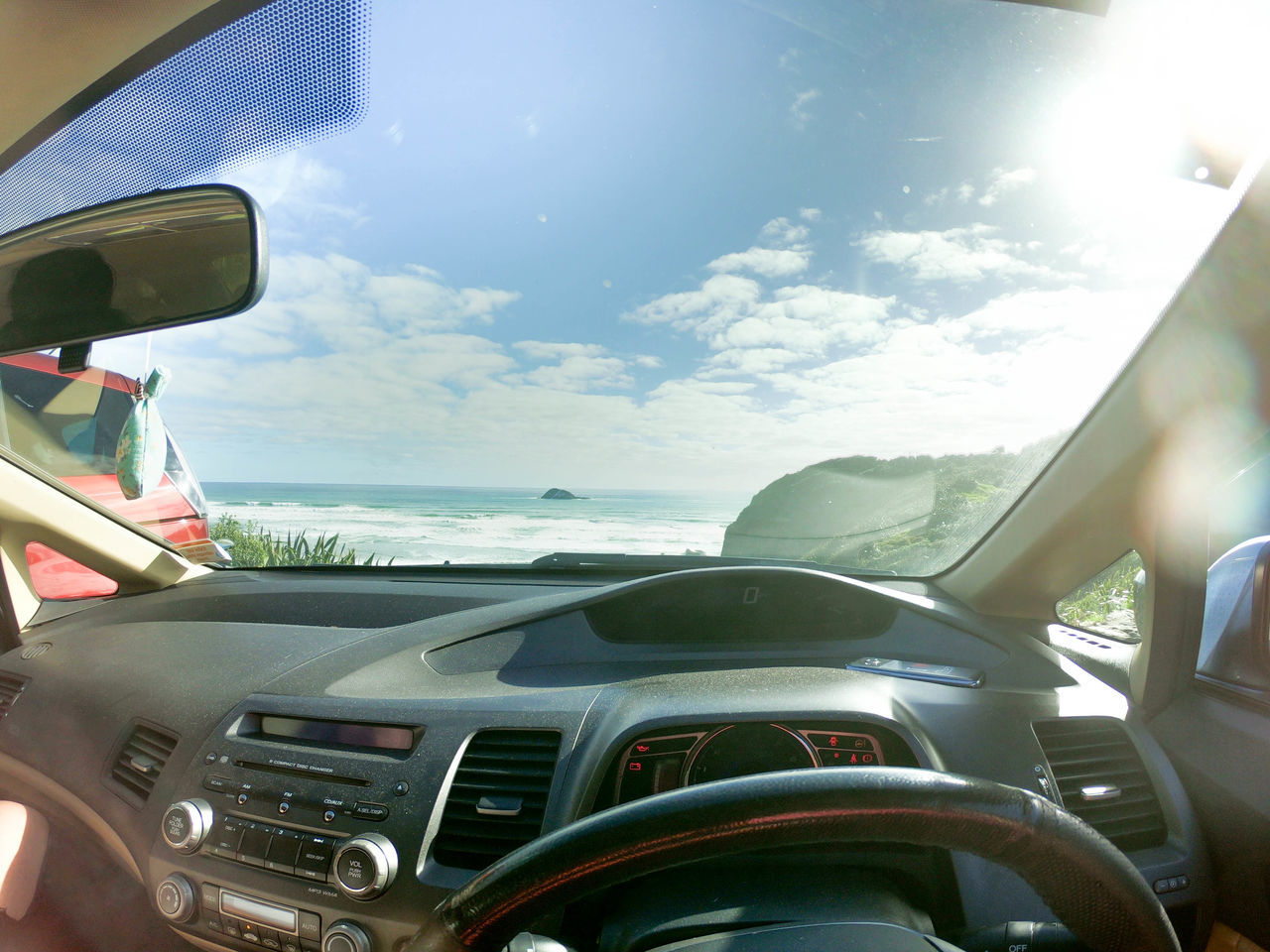 mode of transportation, transportation, car, motor vehicle, vehicle interior, sky, land vehicle, cloud - sky, steering wheel, day, car interior, sunlight, glass - material, windshield, nature, control panel, dashboard, travel, sea, transparent, no people, outdoors, lens flare, road trip