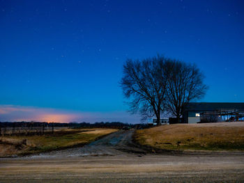 Road by bare trees on field against sky at night