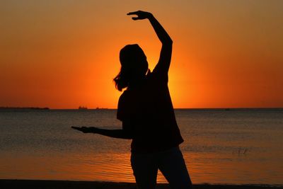 Silhouette woman standing on beach against orange sky