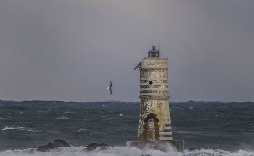 Lighthouse by sea against sky