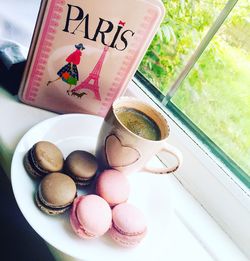 Tilt image of macaroons with coffee served on window sill by pink bag