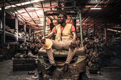 Full length of worker sitting on forklift at factory