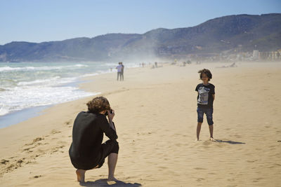 Rear view of woman photographing son at beach