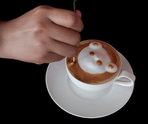 Cropped image of hand holding coffee cup against black background