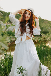 Portrait of beautiful young woman standing by plants against sky