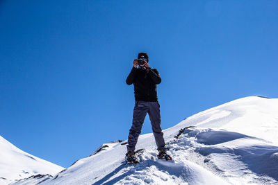 Low angle view of person photographing against clear blue sky