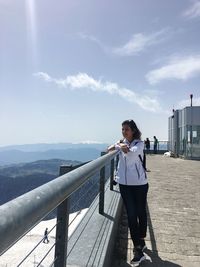 Full length of woman looking at view while standing by railing against blue sky during sunny day