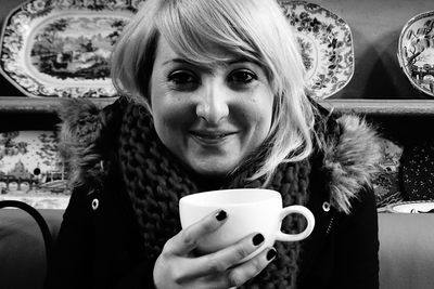 Close-up portrait of smiling young woman with coffee cup