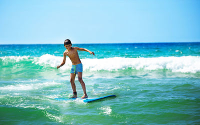 Full length of shirtless man surfing in sea against clear sky