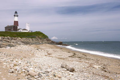 Lighthouse on beach by sea against sky