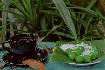 A cup of tea and green klepon cake sprinkled with coconut pulp are placed on the table