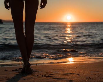Low section of woman standing on beach during sunset