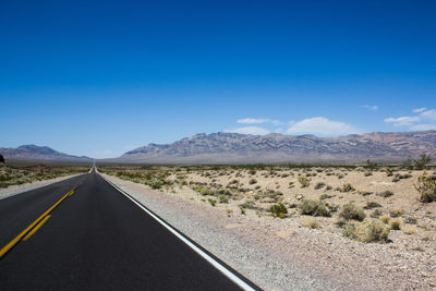 Scenic view of road by desert against blue sky