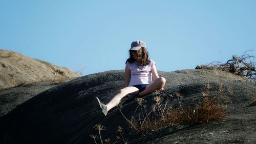 Girl sitting in rock against clear sky