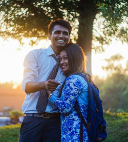 Happy young couple standing at park during sunset