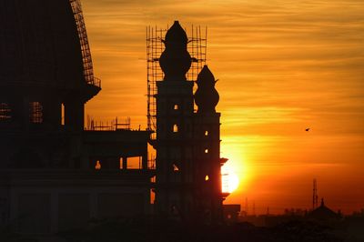 Silhouette built structure against orange sky