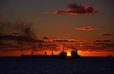 Silhouette boats in sea against orange sky during sunset