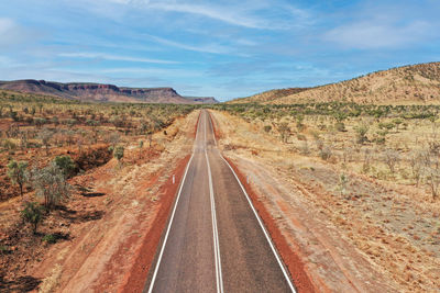 Empty road leading towards mountain against sky