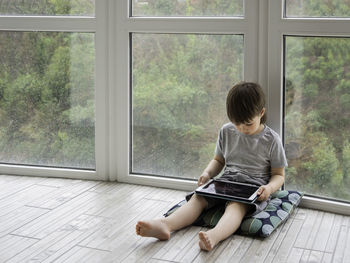 Curious boy watch cartoons on digital tablet. kid sits on floor, uses electronic device. 