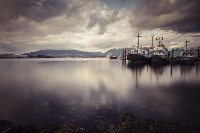 Boats moored at harbor against cloudy sky