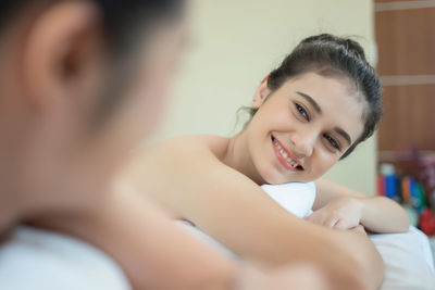 Young woman looking at friend while lying massage table in spa
