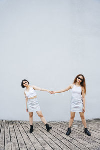 Full length of lesbian couple holding hands standing against wall outdoors