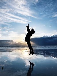 Silhouette woman jumping over sea against sky during sunset