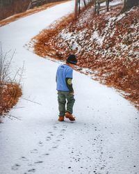 Rear view of boy walking on road during winter