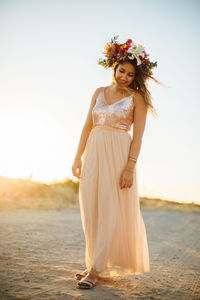 Woman wearing flowers standing at beach against sky