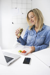 Smiling businesswoman eating food while sitting in office