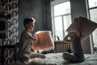 Siblings playing pillow fight at home
