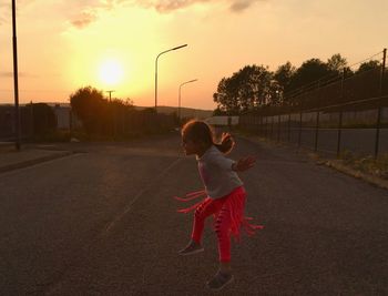 Rear view of girl on road against sky during sunset