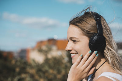 Smiling young woman listening to music against sky