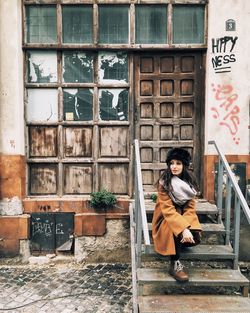 Woman looking away while sitting on steps against built structure