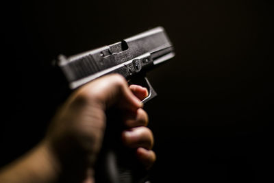 Cropped hand holding gun against black background