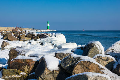 Frozen rocks at beach against clear sky