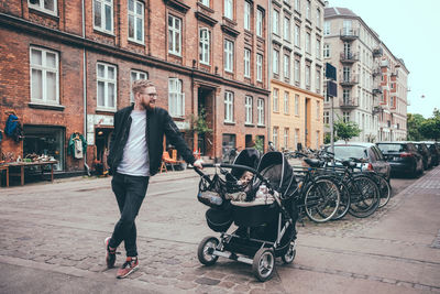 Full length of father standing by baby carriage on street in city