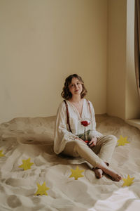 Young female in victorian shirt sitting with rose on the sand and smile