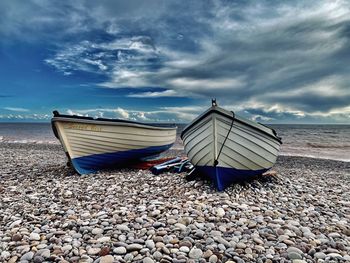 Boats and pebbles on beach against sky