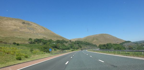 Empty road by mountain against blue sky