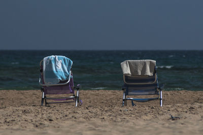 Rear view of chairs on beach against clear sky