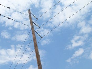 Low angle view of electricity pylon against cloudy sky