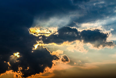 Low angle view of sunlight streaming through clouds