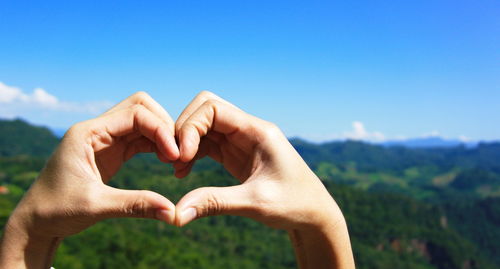 Cropped hands of person making heart shape against sky