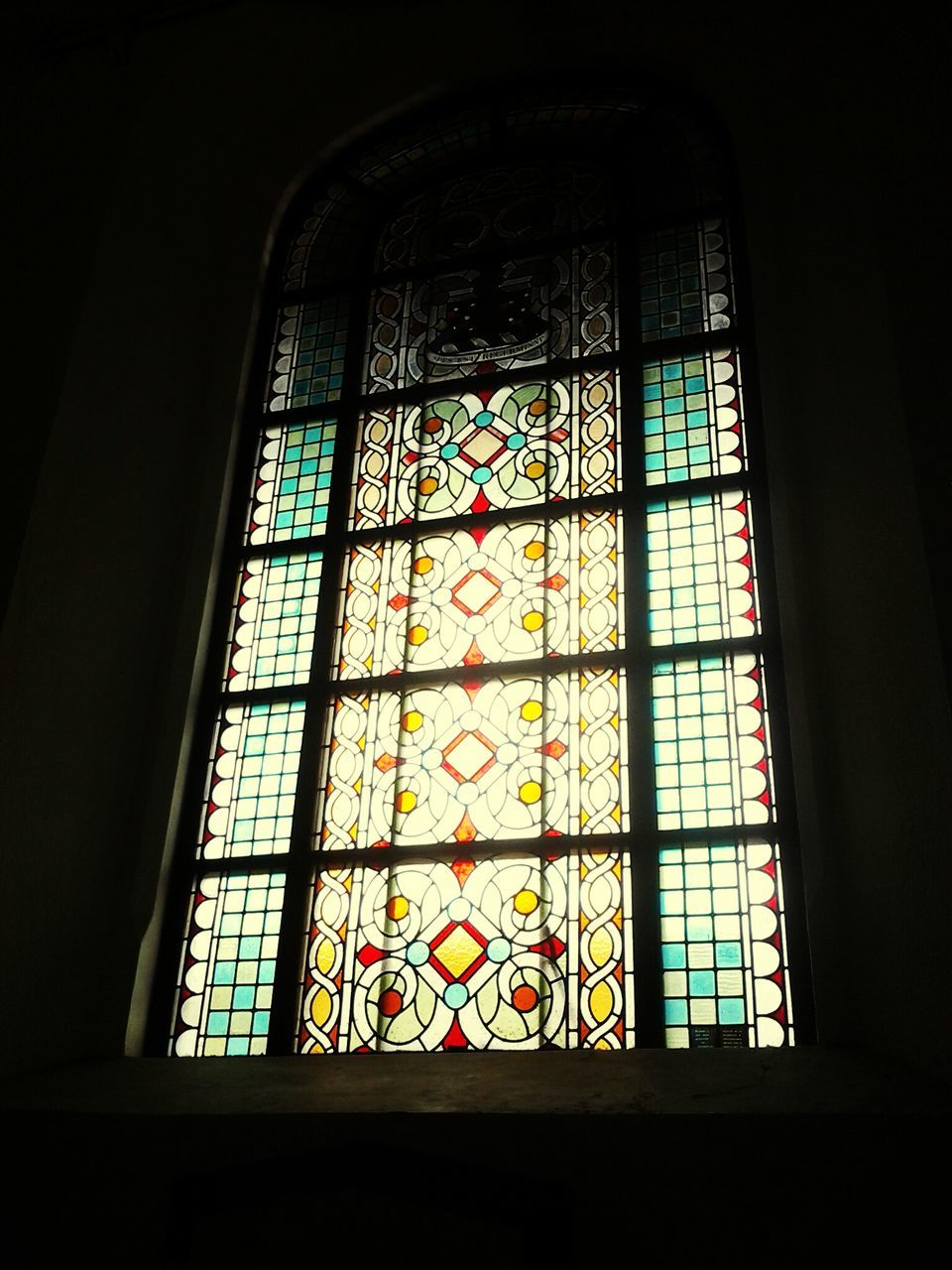 indoors, window, glass - material, architecture, stained glass, built structure, transparent, low angle view, design, pattern, no people, blue, day, geometric shape, church, dark, interior, closed, building, reflection