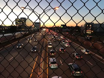 Cars moving on road seen through chainlink fence during sunset