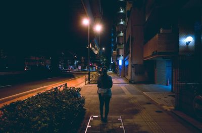 Rear view of woman standing on sidewalk at night