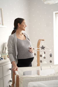 Happy pregnant woman by crib at home