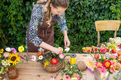 A cute florist girl collects a bouquet in a basket of autumn flowers on her desktop